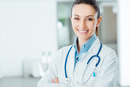 Confident female doctor posing in her office and smiling at camera, health care and prevention concept