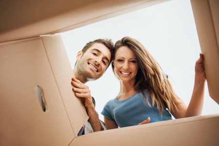 Smiling young couple opening a carton box and looking inside, relocation and unpacking concept Smiling young couple opening a carton box and looking inside, relocation and unpacking concept