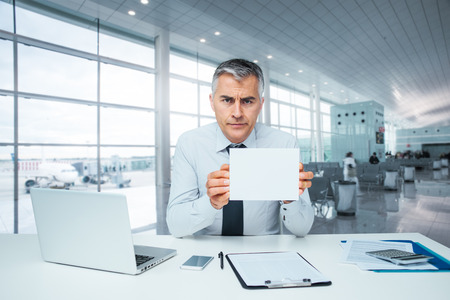 Frowning bank clerk at desk holding a sign and rejecting a loan applicationの写真素材