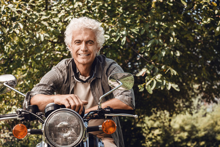 Confident handsome man riding a vintage motorbike and smiling at cameraの写真素材