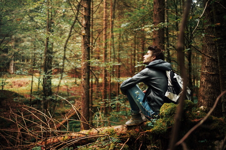 Young man sitting on a trunk in the forest and relaxing, freedom and individuality concept