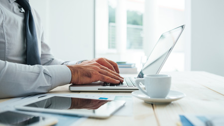 Professional businessman working at office desk and typing on a laptop, unrecognizable person