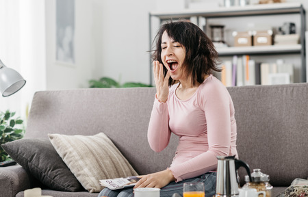 Young woman at home waking up after a bad night's sleep on the couch, she is yawningの写真素材