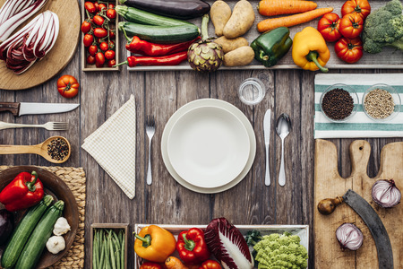 Fresh healthy vegetables, chopping boards and cooking utensils composing a frame on a vintage kitchen worktop, table set at centerの写真素材