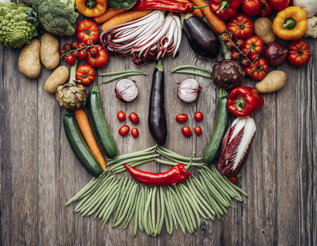 Smiling face of a man with beard made with fresh colorful vegetables on a rustic wooden worktopの写真素材