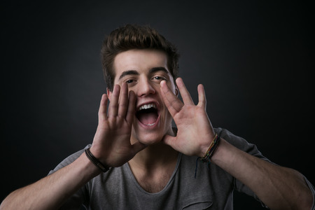 Attractive young man shouting out loud with hands around mouthの写真素材