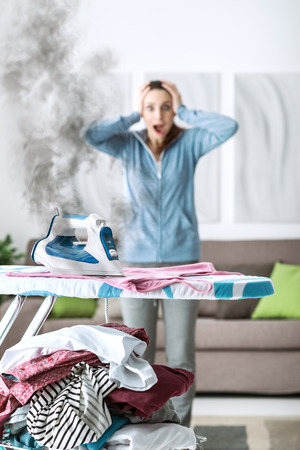 Shocked woman gasping at home, she has left the iron on and she is burning her clothesの写真素材