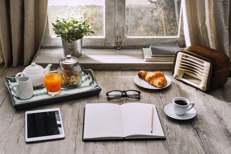 Relaxing healthy breakfast at home: tray, coffee, vintage radio, tablet and a blank open notebook