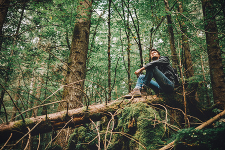 Young man sitting on a trunk in the forest and relaxing, freedom and individuality concept