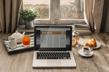 Laptop and coffee on a wooden table in front of a window in a rustic house, hipster breakfast conceptの写真素材