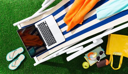 Striped deckchair in the garden with laptop and accessories: summertime, relax and sunbathing