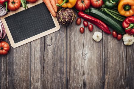 Fresh colorful organic vegetables on a wooden table and blank blackboard, agriculture and healthy eating conceptの写真素材