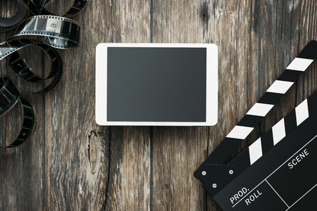 Digital tablet, clapper and filmstrip on a wooden desktop: cinema and entertainment conceptの写真素材
