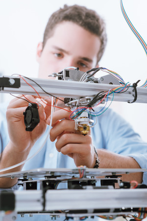 Young engineer in the laboratory working on a 3D printer and checking wires, education and...