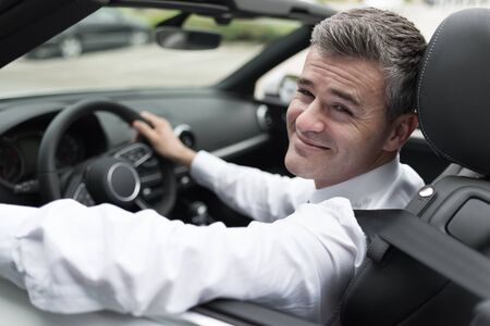 Successful confident businessman driving to work with his brand new expensive car, he is smiling at cameraの写真素材