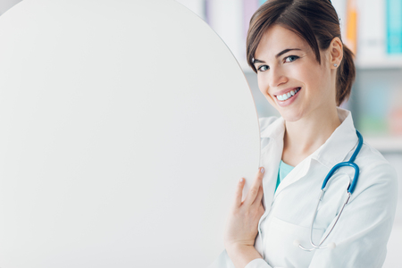 Smiling female doctor holding a round white sign, blank copy space, healthcare conceptの写真素材