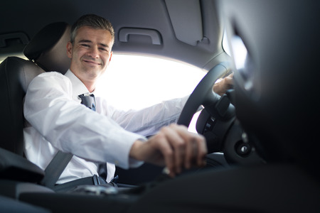Confident smiling businessman driving to work with his brand new car, business and luxury conceptの写真素材