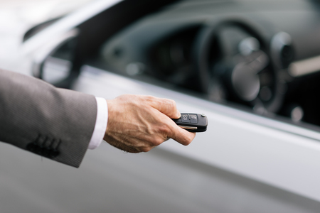 Businessman holding a car key with remote control and pushing a button, he is unlocking the door, hand close upの写真素材