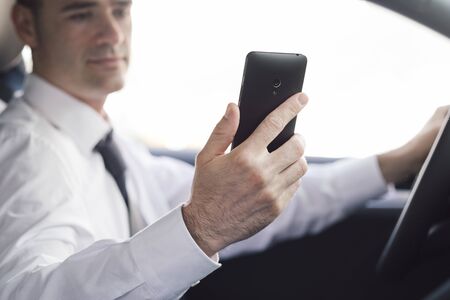 Businessman driving his car and using mobile apps on his smartphone, navigation and technology...