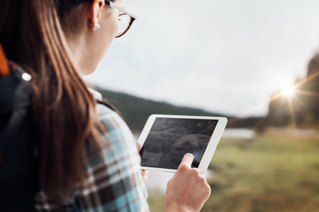 Young female hiker walking in nature and connecting with a digital tablet, technology and...
