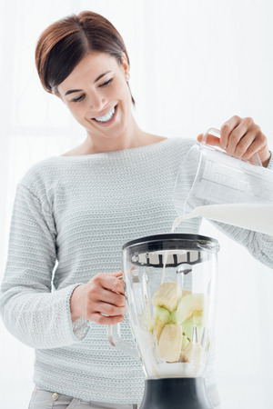 Woman preparing an healthy smoothie with bananas, she is pouring milk into a blender and smilingの写真素材