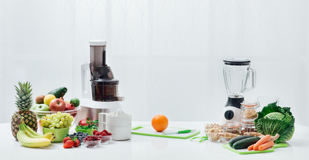 Kitchen table with fresh vegetables, fruit, seeds, blender and juicers; healthy diet and food preparation conceptの写真素材