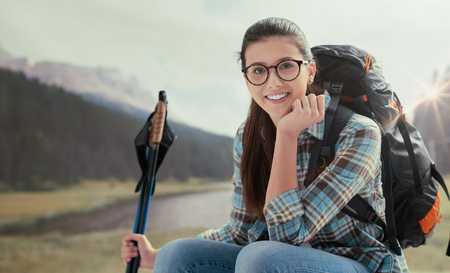 Young smiling woman trekking on the mountains and having a relaxing break, she is sitting and holding hiking polesの写真素材
