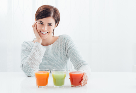 Smiling young woman having natural healthy drinks for her diet: red, green and orange juiceの写真素材