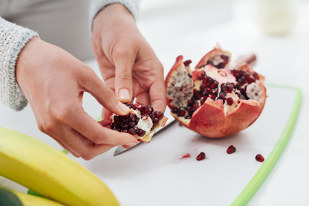 Woman preparing food in her kitchen, she is opening a ripe juicy pomegranate with her handsの写真素材
