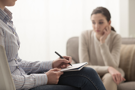 Psychologist listening to her patient and writing down notes, mental health and counseling conceptの写真素材