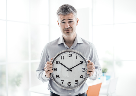 Business, time management and deadlines: sad businessman holding a clock, he is missing a deadline