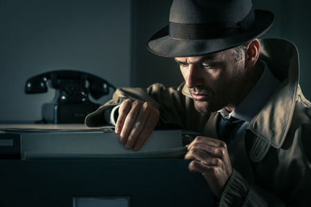 Vintage undercover criminal spy stealing files in a filing cabinet late at night, security and data theft conceptの写真素材