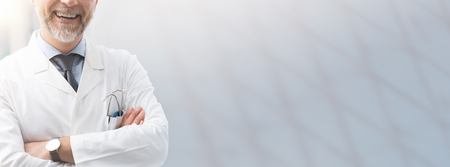 Confident smiling doctor posing with arms crossed and blank copy space, healthcare and health insurance bannerの写真素材