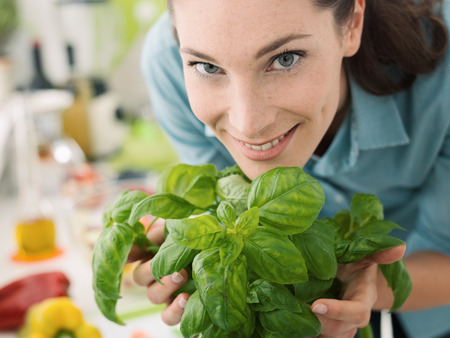 Smiling woman smelling fresh basil at home and preparing healthy food in the kitchenの写真素材