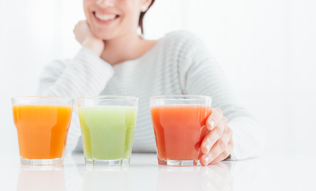 Smiling young woman having natural healthy drinks for her diet: red, green and orange juiceの写真素材