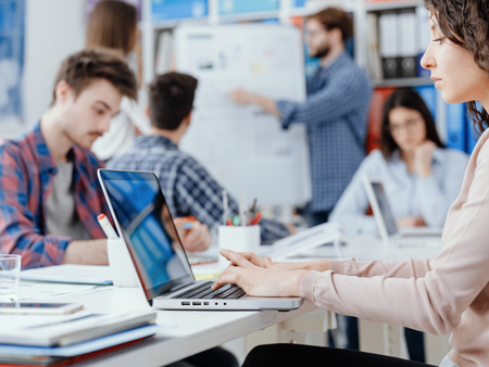 Young business team meeting in the office and working, a woman is using a laptop on the foreground:...