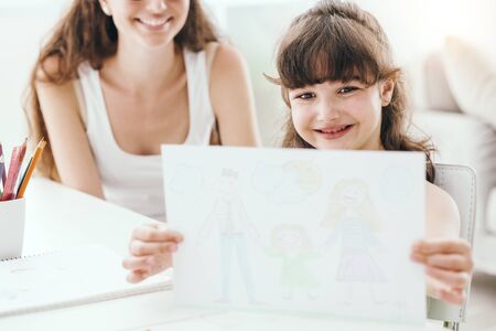 Cheerful cute girl holding a blank sign and smiling, her mother is sitting behind herの写真素材