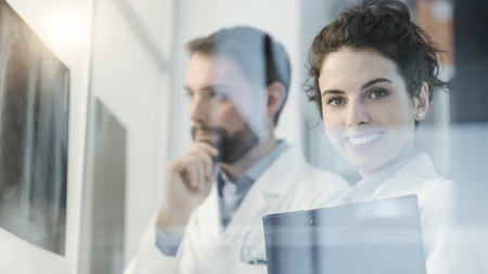 Professional doctors examining a patient's x-ray and discussing, a young practitioner is smiling at cameraの写真素材