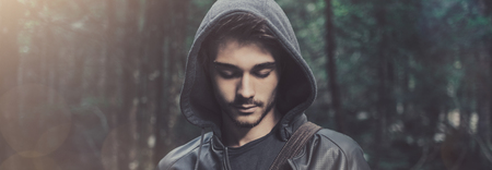 Young hooded cool man in the woods looking down, wild forest on backgroundの写真素材