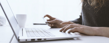 Woman doing online shopping using her laptop and a credit card, hands close up, e-commerce and online banking conceptの写真素材