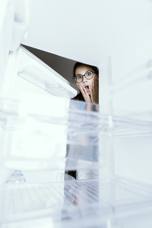 Young hungry desperate woman looking into her empty fridge, she is panickingの写真素材