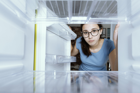 Sad woman looking into her empty fridge with no groceriesの写真素材