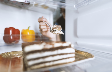 Hungry woman eating a dessert straight from the fridge using a fork, diet fail conceptの写真素材
