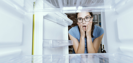 Young hungry desperate woman looking into her empty fridge, she is panickingの写真素材