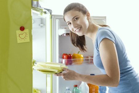 Smiling woman taking some fresh celery from the fridge and preparing an healthy meal at homeの写真素材