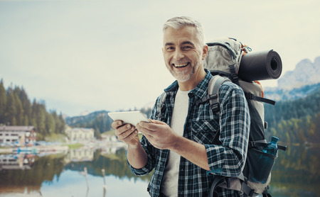 Hiker trekking on the mountains and connecting with a digital touch screen tablet using an outdoor wireless access pointの写真素材