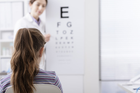 Oculist testing a young patient's eyesight using an eye chart, ophthalmology and eyesight conceptの写真素材
