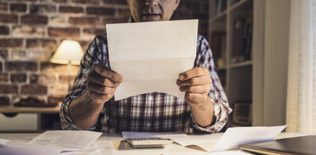 Concerned sad man checking his domestic bills, he has too many expensesの写真素材