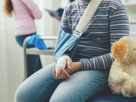 Cute girl in the doctor's office waiting to be visited, she is sitting on the examination couch with her teddy bearの写真素材