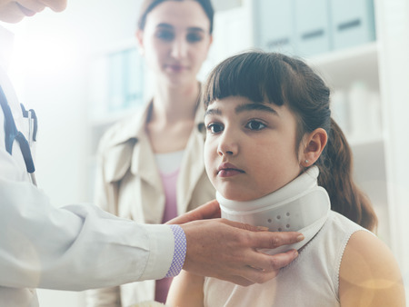 Doctor visiting a young girl with orthopedic cervical collar, first aid and treatment conceptの写真素材